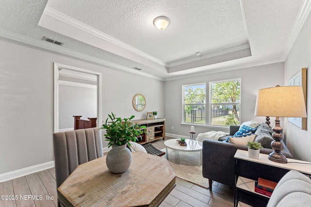 living area featuring light wood-style flooring, visible vents, a textured ceiling, and a tray ceiling