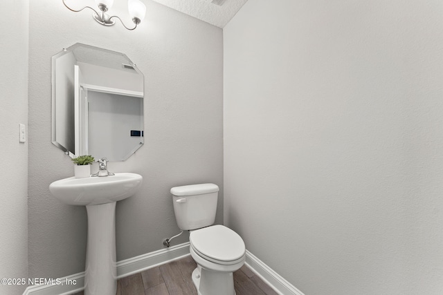 half bathroom with wood finished floors, toilet, and baseboards