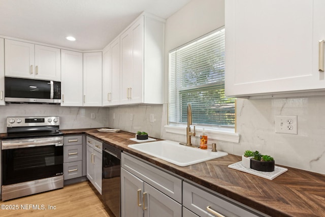 kitchen with butcher block countertops, a sink, white cabinetry, and stainless steel appliances
