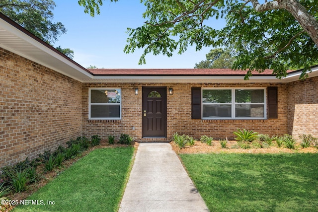 entrance to property with brick siding and a lawn