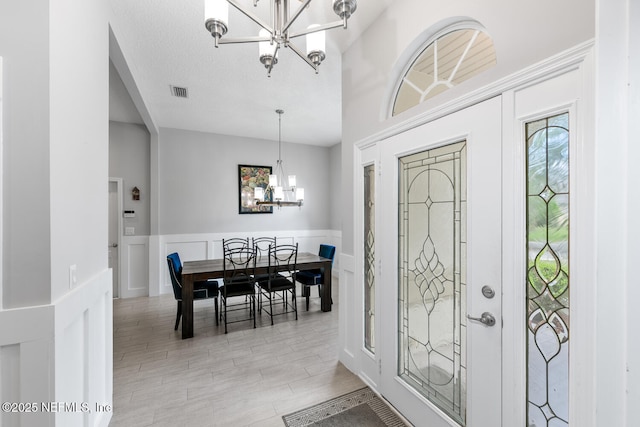 entryway with a decorative wall, a textured ceiling, visible vents, a wainscoted wall, and a notable chandelier