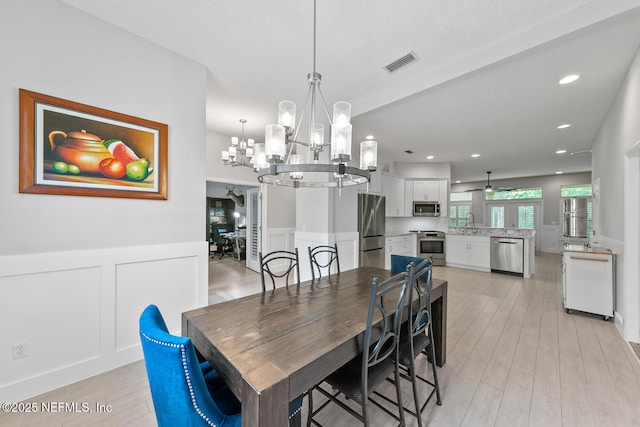 dining space featuring a chandelier, a wainscoted wall, visible vents, a decorative wall, and light wood finished floors