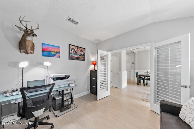 home office featuring a textured ceiling, light wood finished floors, lofted ceiling, and visible vents
