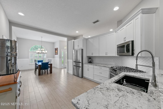 kitchen with light stone counters, a chandelier, wainscoting, visible vents, and appliances with stainless steel finishes