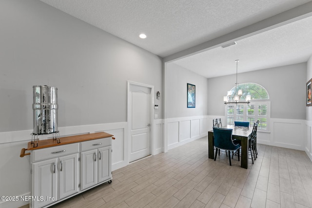 dining space with a notable chandelier, light wood-type flooring, a textured ceiling, a wainscoted wall, and visible vents