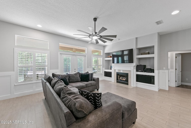 living area featuring visible vents, built in features, ceiling fan, a textured ceiling, and light wood-style flooring
