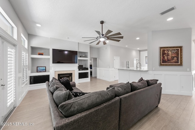 living area featuring a decorative wall, visible vents, built in features, and a textured ceiling