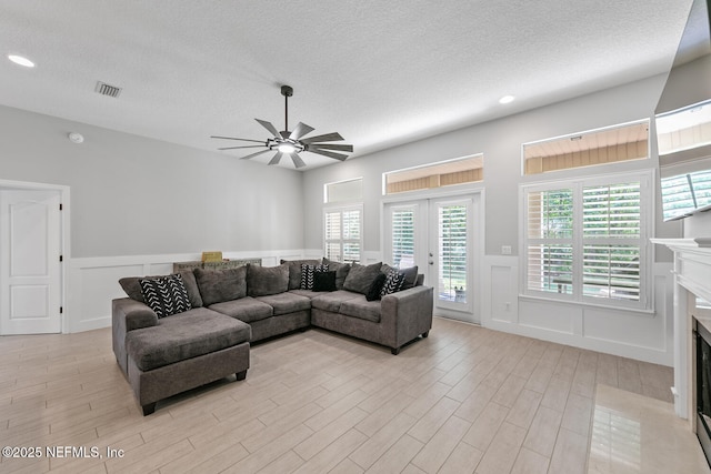 living room with a fireplace with flush hearth, light wood-type flooring, ceiling fan, and visible vents