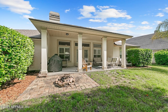 back of property with a chimney, a patio area, stucco siding, and a yard