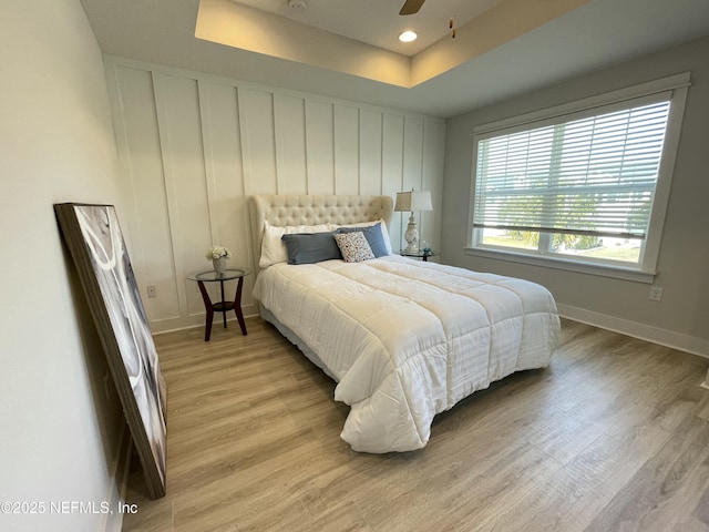 bedroom featuring baseboards, recessed lighting, a ceiling fan, light wood-type flooring, and a tray ceiling