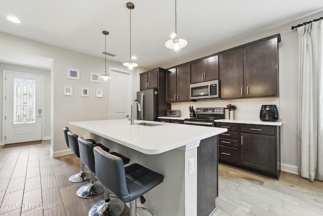 kitchen with a kitchen bar, dark brown cabinetry, appliances with stainless steel finishes, and a kitchen island with sink