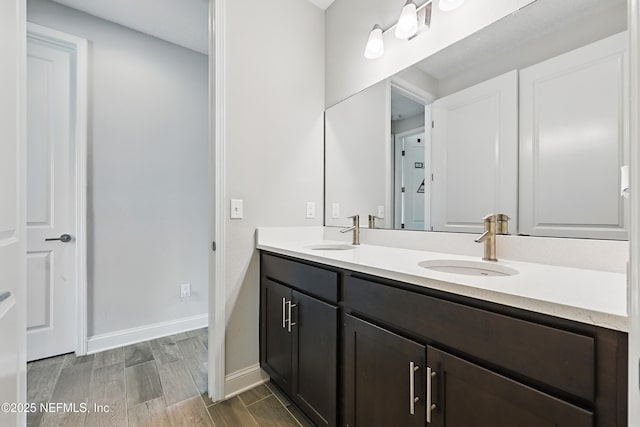 full bath featuring baseboards, wood finished floors, a sink, and double vanity
