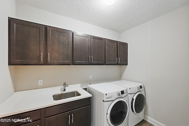 clothes washing area with a sink, a textured ceiling, washer and dryer, cabinet space, and baseboards