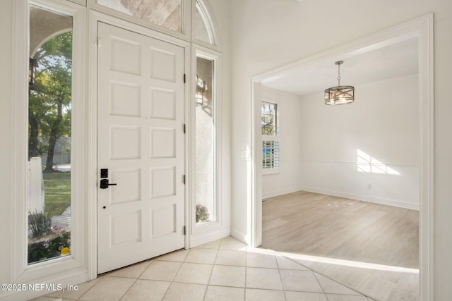 foyer featuring light tile patterned flooring, plenty of natural light, baseboards, and a notable chandelier