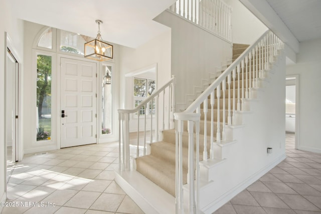 tiled entryway with stairway, an inviting chandelier, and baseboards