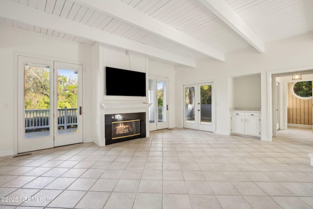 unfurnished living room featuring beamed ceiling, a glass covered fireplace, plenty of natural light, and french doors