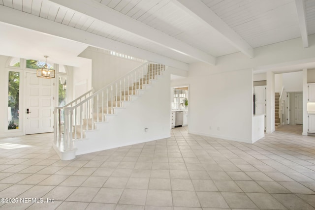 unfurnished living room with light tile patterned floors, beamed ceiling, baseboards, a chandelier, and stairs