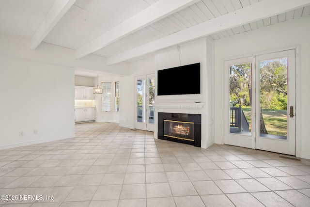 unfurnished living room featuring baseboards, a glass covered fireplace, beam ceiling, and a healthy amount of sunlight