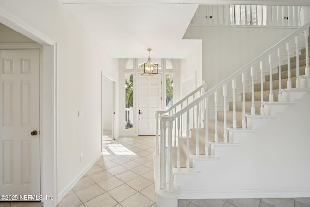 tiled foyer with a chandelier, stairway, baseboards, and plenty of natural light