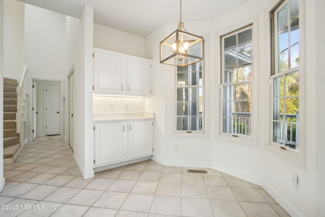 unfurnished dining area with stairway, a wealth of natural light, light tile patterned floors, and an inviting chandelier