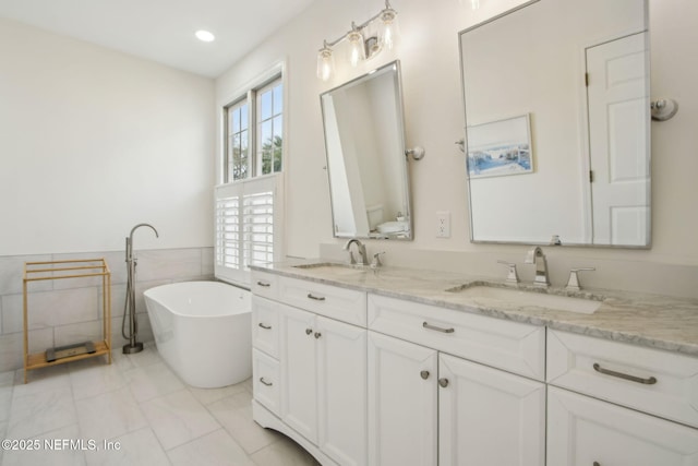 bathroom featuring a soaking tub, tile walls, a sink, and double vanity
