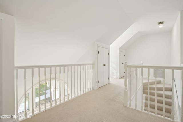 hall featuring an upstairs landing, carpet floors, vaulted ceiling, and visible vents