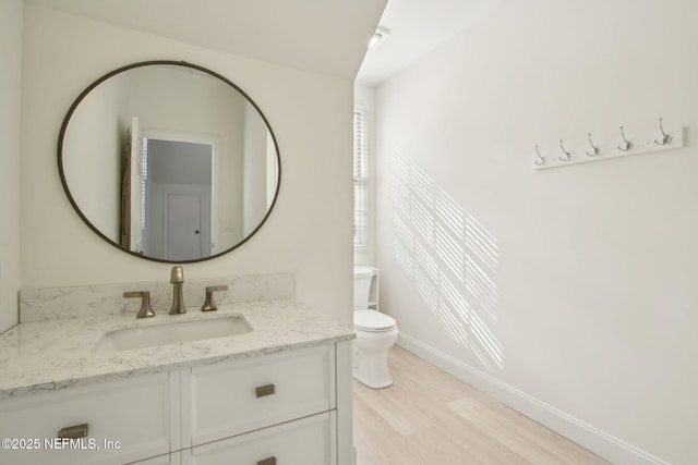 bathroom featuring baseboards, wood finished floors, toilet, and vanity