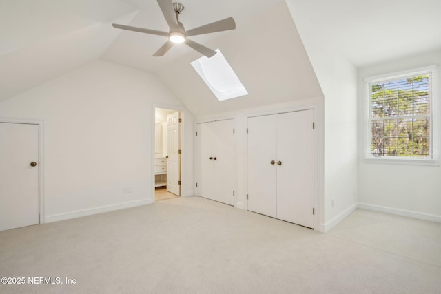 additional living space with baseboards, lofted ceiling with skylight, light colored carpet, and ceiling fan
