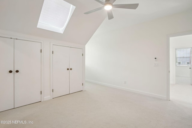 unfurnished bedroom with multiple closets, baseboards, lofted ceiling with skylight, and light colored carpet