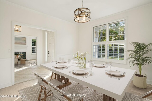 dining area featuring light wood-style flooring, a glass covered fireplace, a chandelier, and crown molding