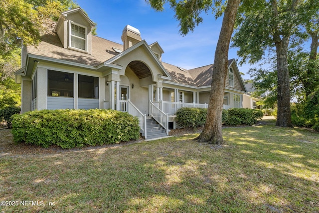 view of front of house with a porch, a shingled roof, a front lawn, and a chimney
