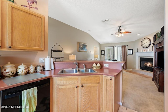 kitchen featuring vaulted ceiling, a tiled fireplace, open floor plan, a peninsula, and a sink