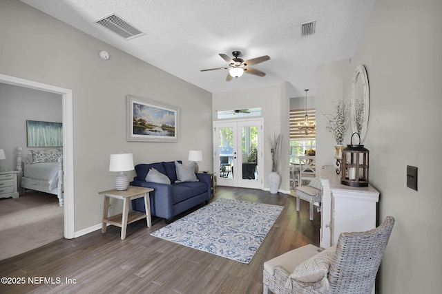 living room with a textured ceiling, dark wood-style floors, visible vents, and ceiling fan with notable chandelier