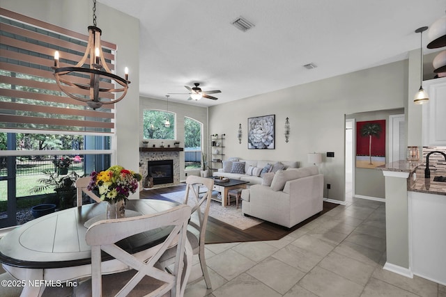 living area featuring baseboards, visible vents, a glass covered fireplace, and ceiling fan with notable chandelier