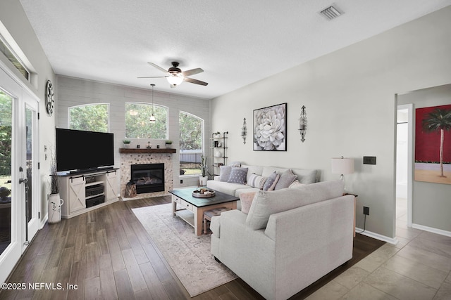 living room with a ceiling fan, a glass covered fireplace, a textured ceiling, dark wood-style floors, and visible vents