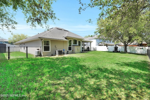 rear view of house featuring a fenced backyard, central AC, a yard, and a shingled roof