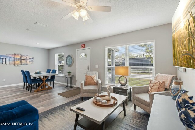 living area with a textured ceiling, a wealth of natural light, wood finished floors, and ceiling fan