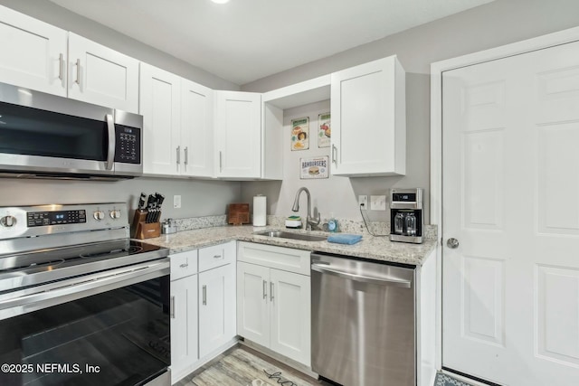 kitchen featuring white cabinetry, a sink, stainless steel appliances, and light stone countertops