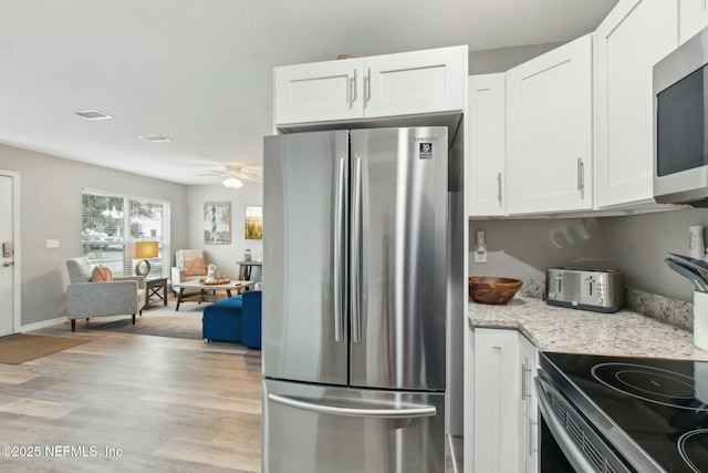 kitchen with a ceiling fan, white cabinetry, light stone countertops, appliances with stainless steel finishes, and light wood-style floors