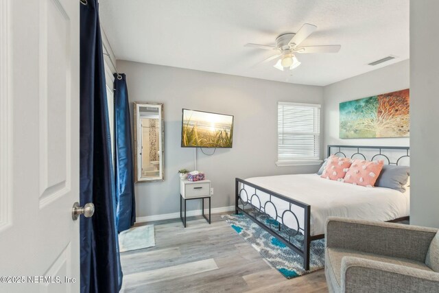 bedroom with a ceiling fan, visible vents, baseboards, and wood finished floors