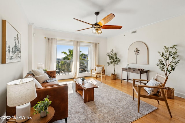 living room featuring wood finished floors, a ceiling fan, visible vents, and crown molding