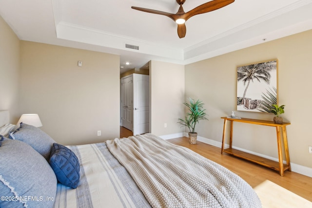 bedroom featuring ornamental molding, wood finished floors, visible vents, and a raised ceiling