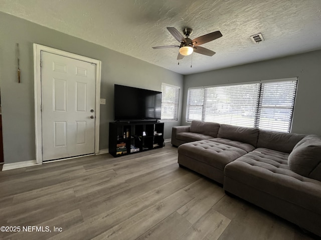living room featuring a textured ceiling, a ceiling fan, visible vents, wood finished floors, and baseboards