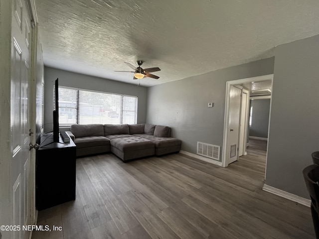 living room featuring a textured ceiling, a ceiling fan, visible vents, wood finished floors, and baseboards
