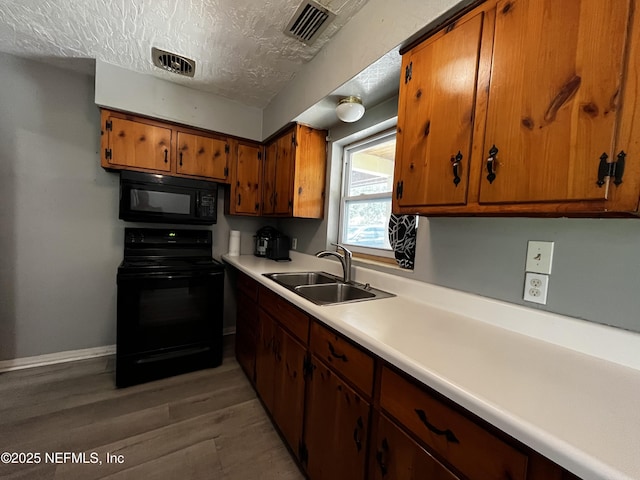 kitchen with brown cabinetry, light wood-type flooring, visible vents, black appliances, and a sink