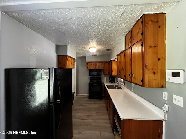 kitchen featuring light countertops, black appliances, brown cabinetry, dark wood finished floors, and a sink