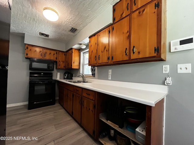 kitchen featuring a textured ceiling, black appliances, visible vents, brown cabinets, and a sink