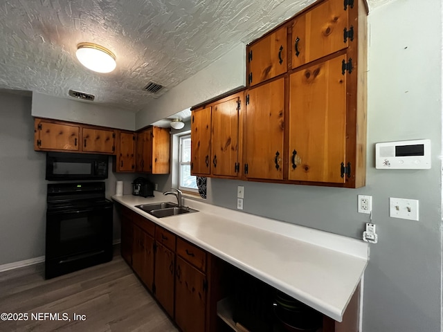 kitchen with light wood-type flooring, light countertops, black appliances, brown cabinets, and a sink