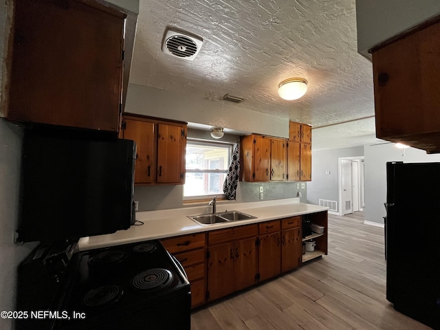 kitchen featuring a sink, visible vents, black appliances, and brown cabinets