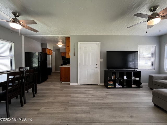 living room with light wood-type flooring, a ceiling fan, plenty of natural light, and a textured ceiling